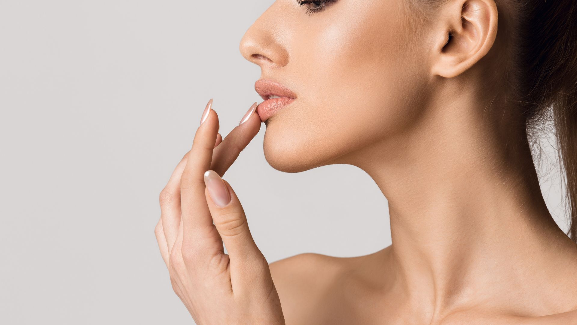 Side profile of woman touching lips with soft, neutral makeup