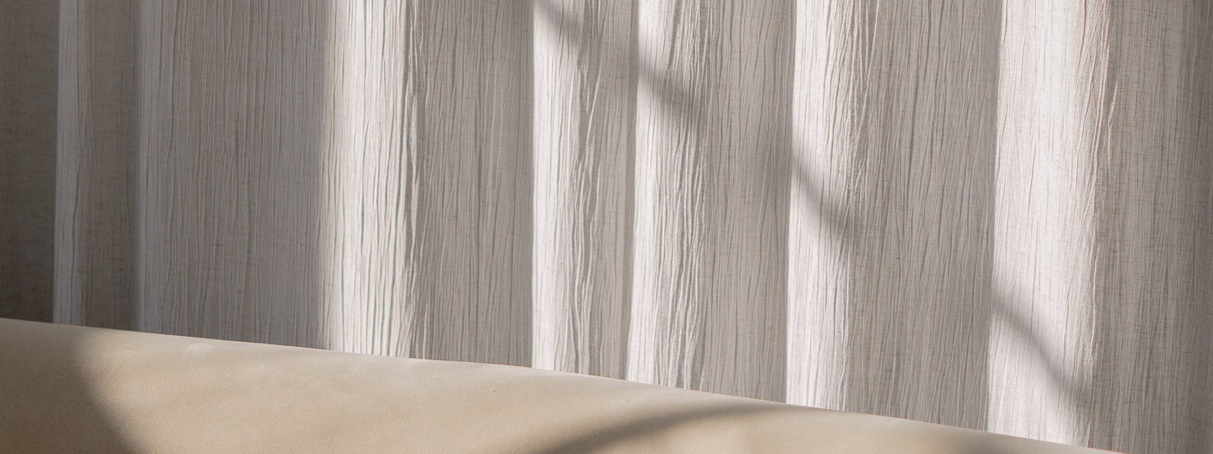 Soft light filtering through wrinkled white curtains onto beige surface